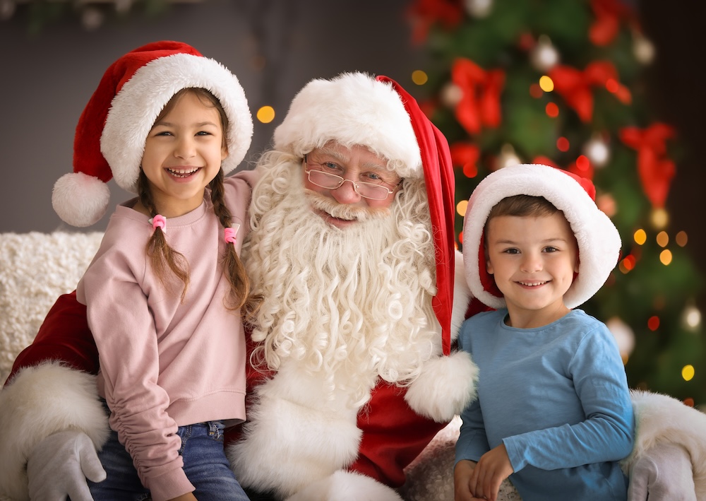 Little children sitting on authentic Santa Claus' knees indoors.